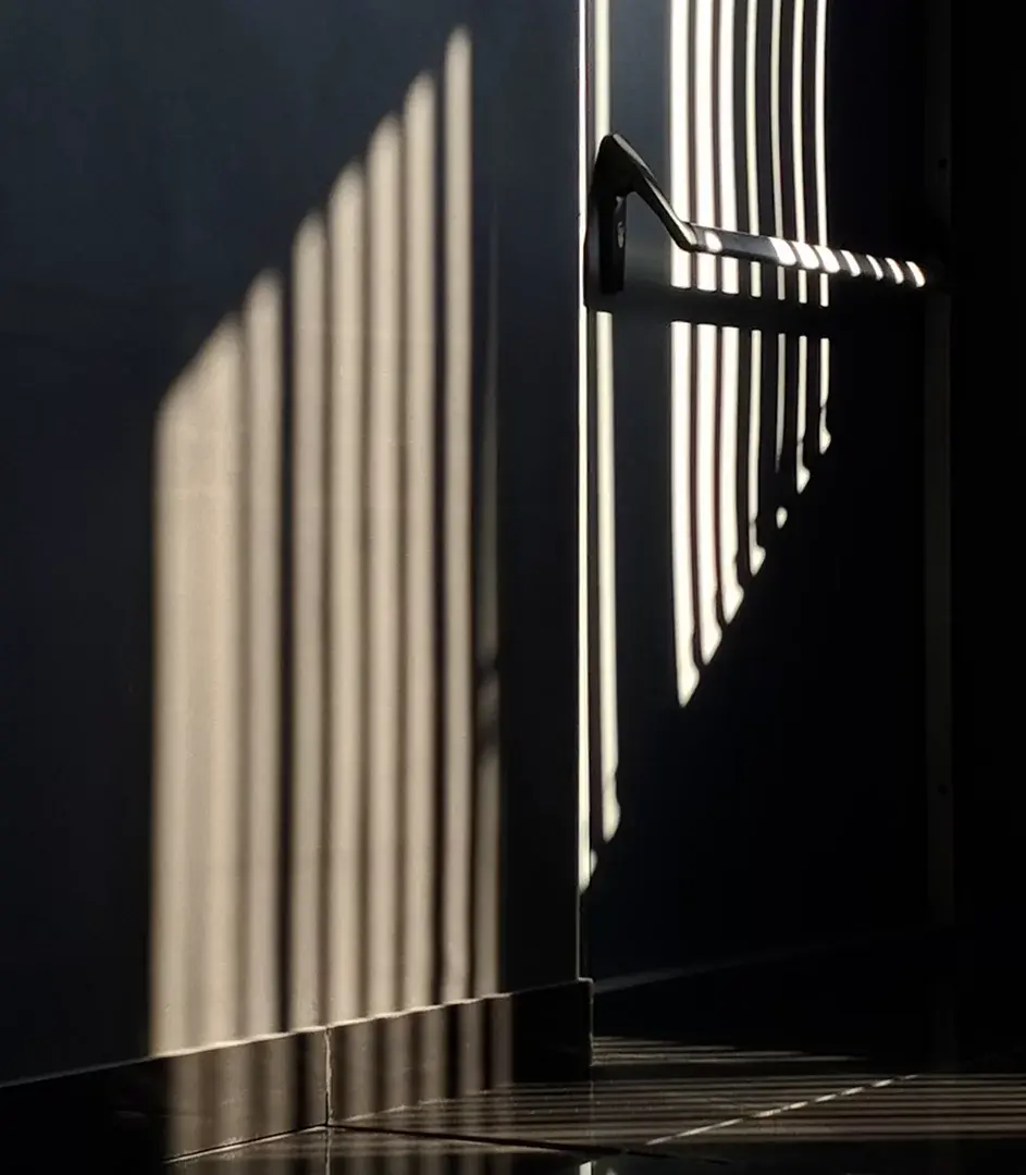 Sunlight through blinds casting striped shadows over a dark wall and a door